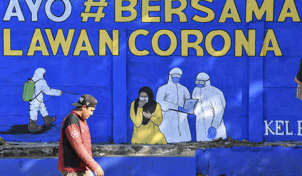 Seorang warga laki-laki Kota Depok berjalan di depan tembok bermural "Ayo Bersama Lawan Corona"