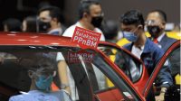 Seorang pria duduk di dalam mobil dengan tulisan mobil ini menerima insentif PPnBM